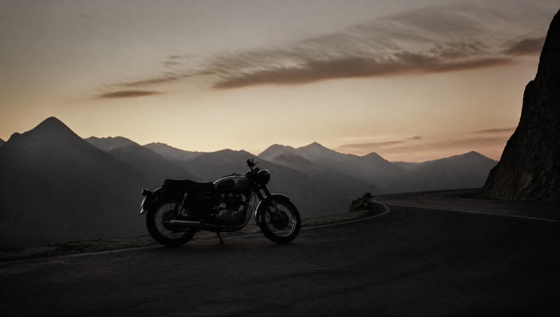 A lone motorcycle silhouetted against a fading sky on an empty alpine road at dusk.