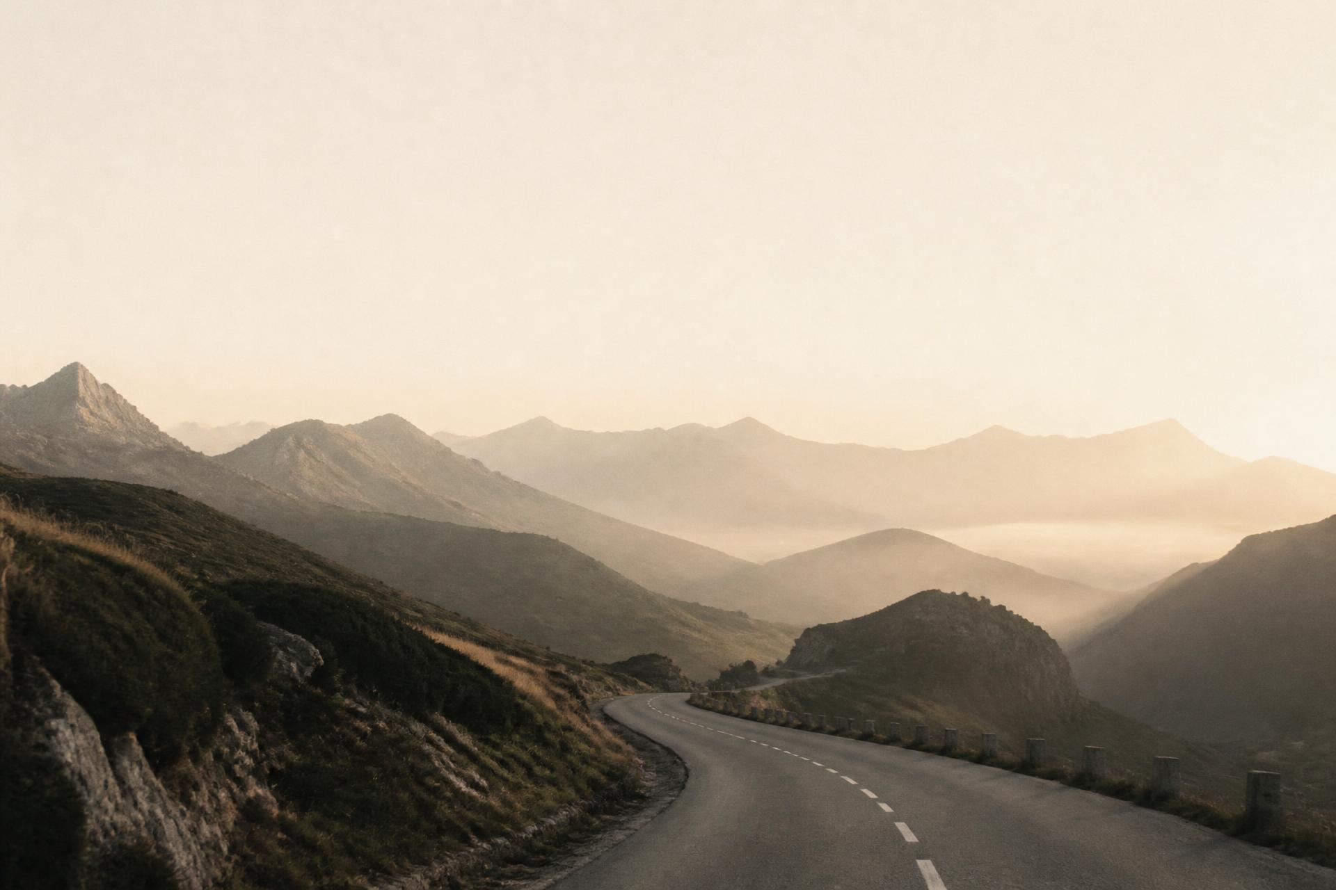 A quiet mountain road at dawn, mist folding between distant ridges.