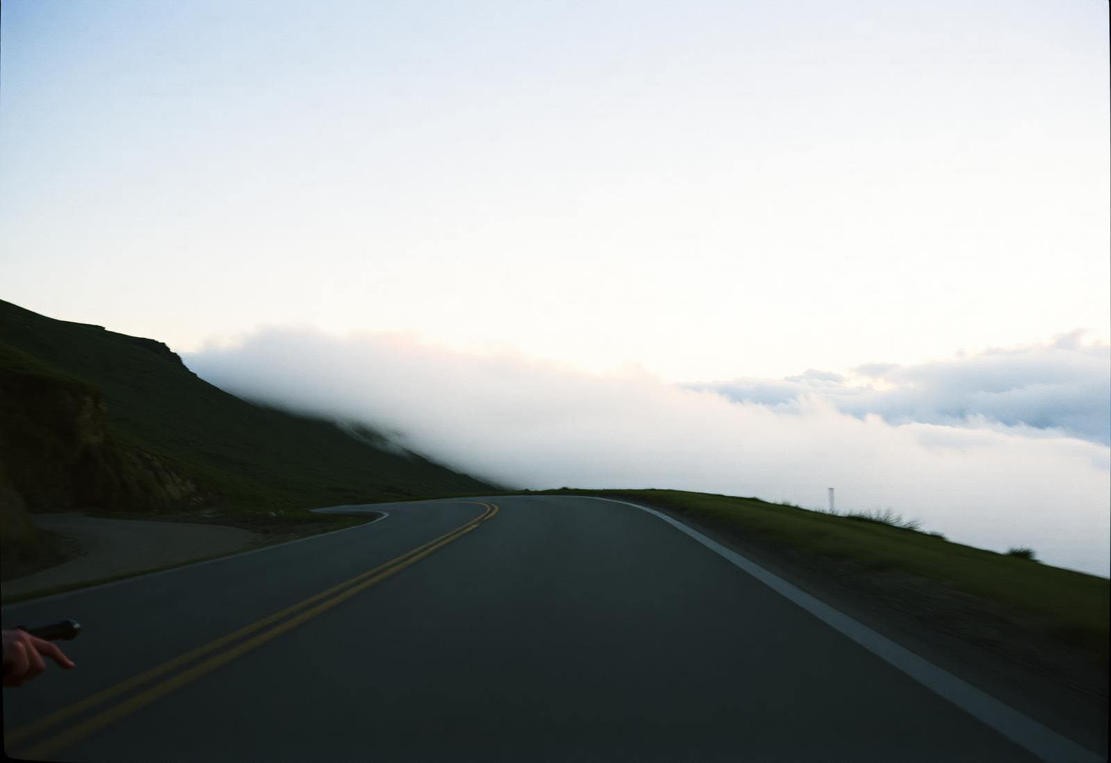 An alpine road curving into low clouds at dawn.